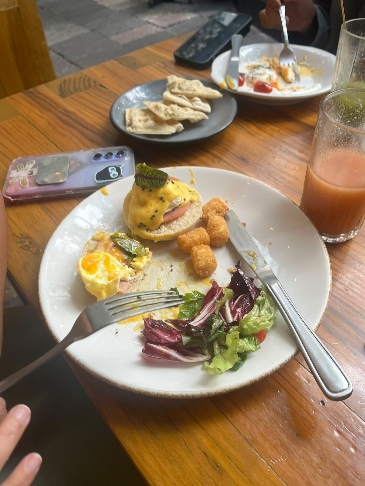 Mesa de desayuno en Frëims con huevos benedictinos, tater tots, ensalada y jugo natural