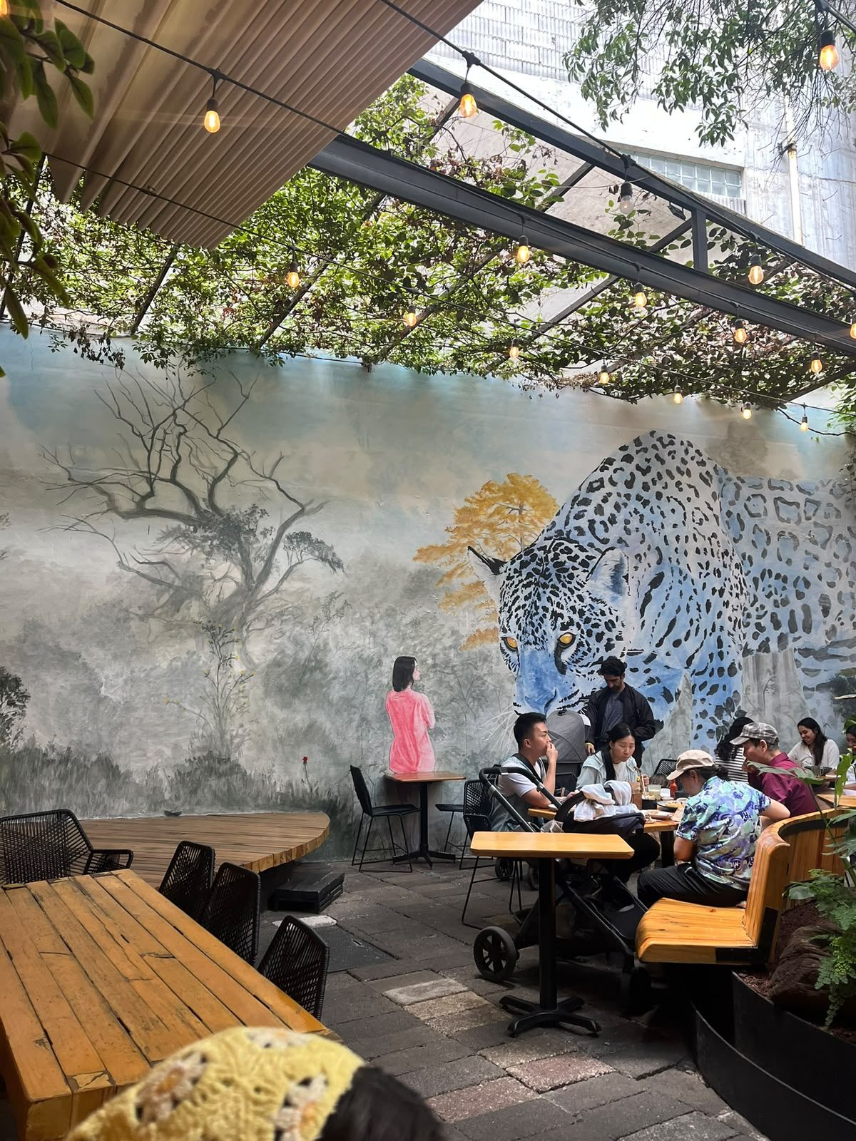 Patio de Frëims con mural de jaguar y mesas entre plantas en la Condesa, CDMX