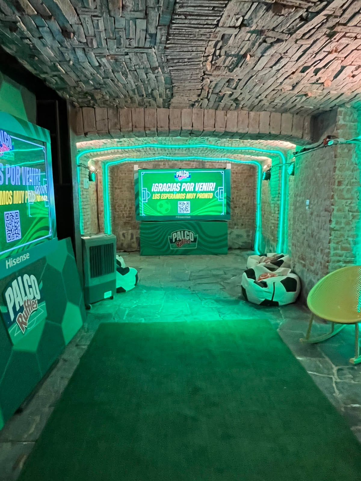 Espacio tipo bóveda del Palco Ruffles con techo de piedra, pantalla Hisense y puffs de balón sobre pasto sintético.