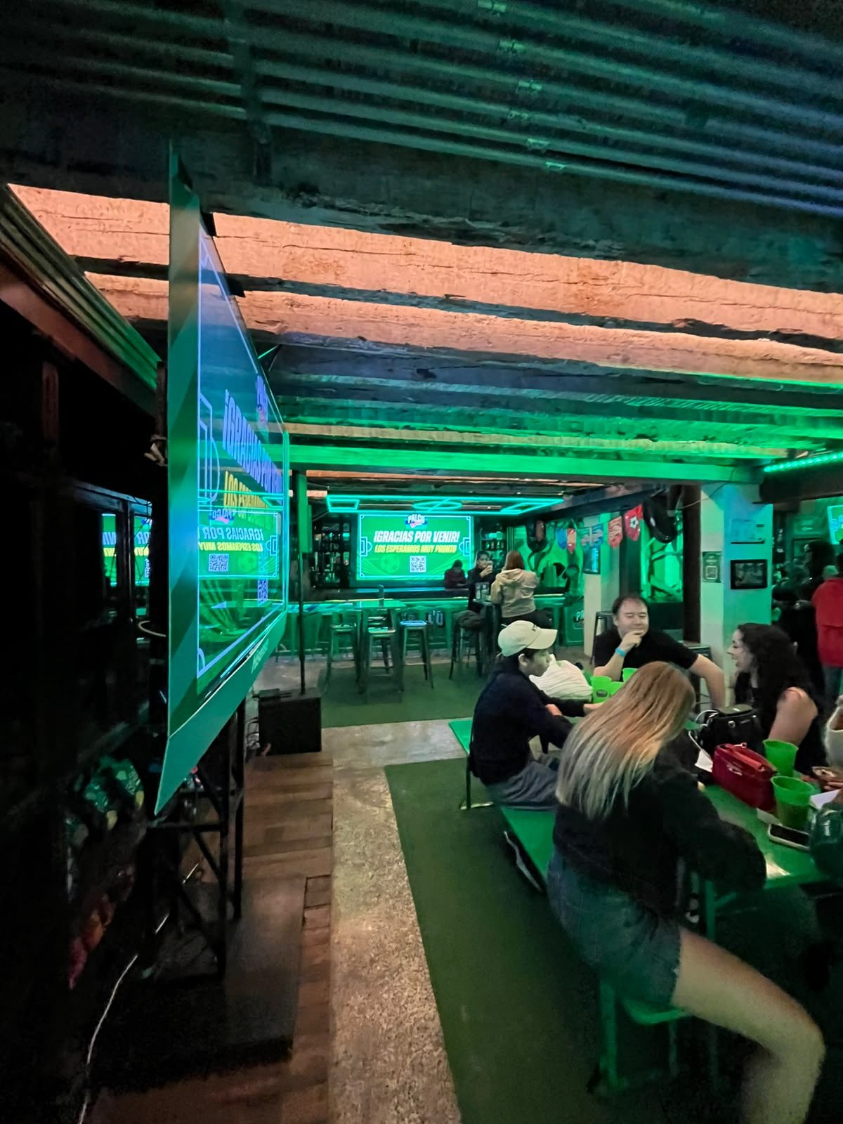 Asistentes conviven en las mesas del patio del Palco Ruffles bajo la iluminación verde del evento.