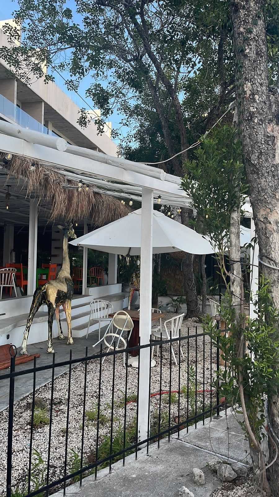 Terraza de un restaurante en Tulum con una jirafa decorativa y las sillas vacías al caer la tarde.