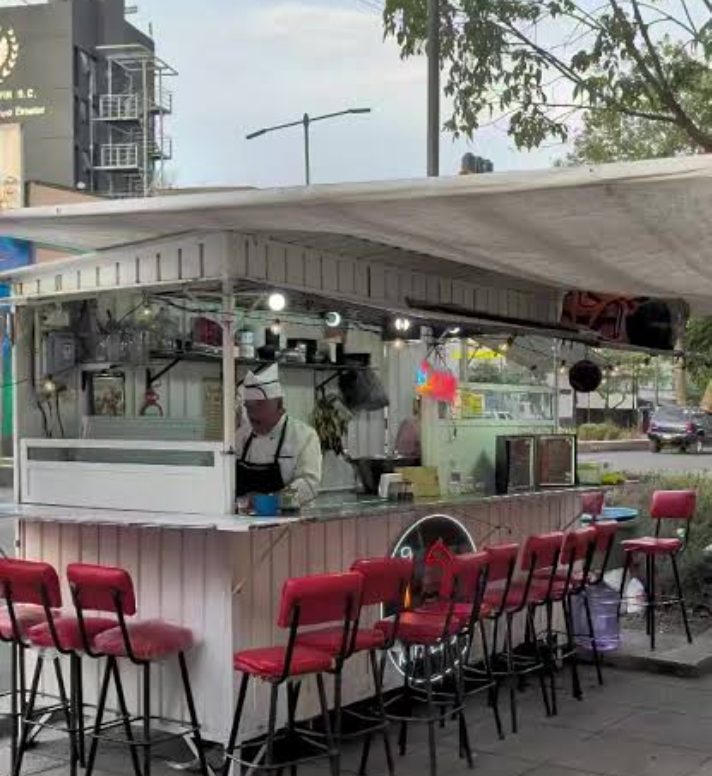 Puesto callejero de Sushi Mickey San en la colonia Doctores, CDMX: caseta blanca con toldo de lona, bancos altos rojos y el cocinero preparando sushi tras la barra