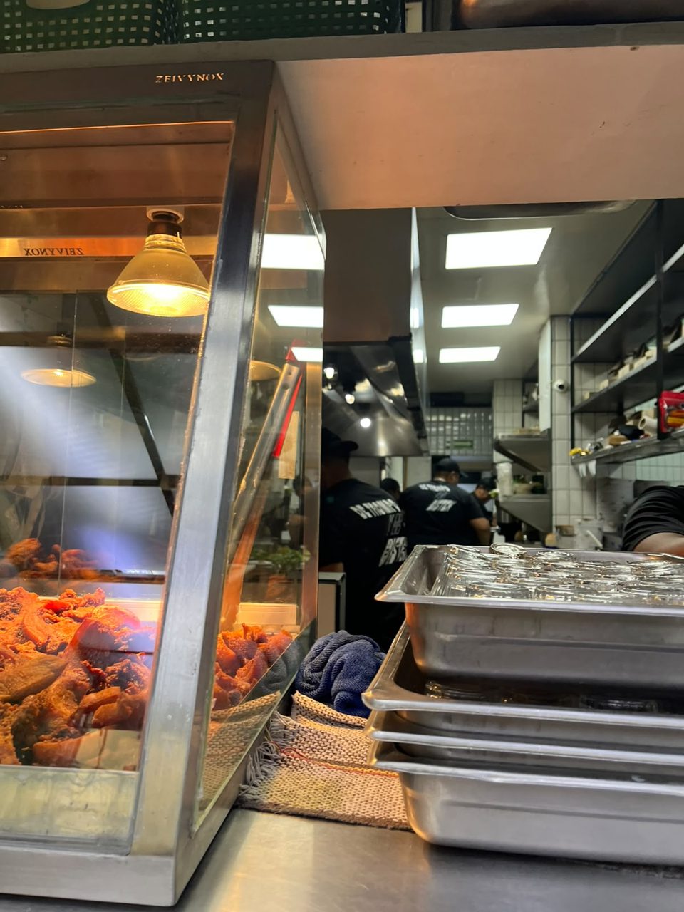 Trompo de al pastor negro asándose bajo la lámpara en la cocina a la vista de Tacos Atarantados, Roma Norte