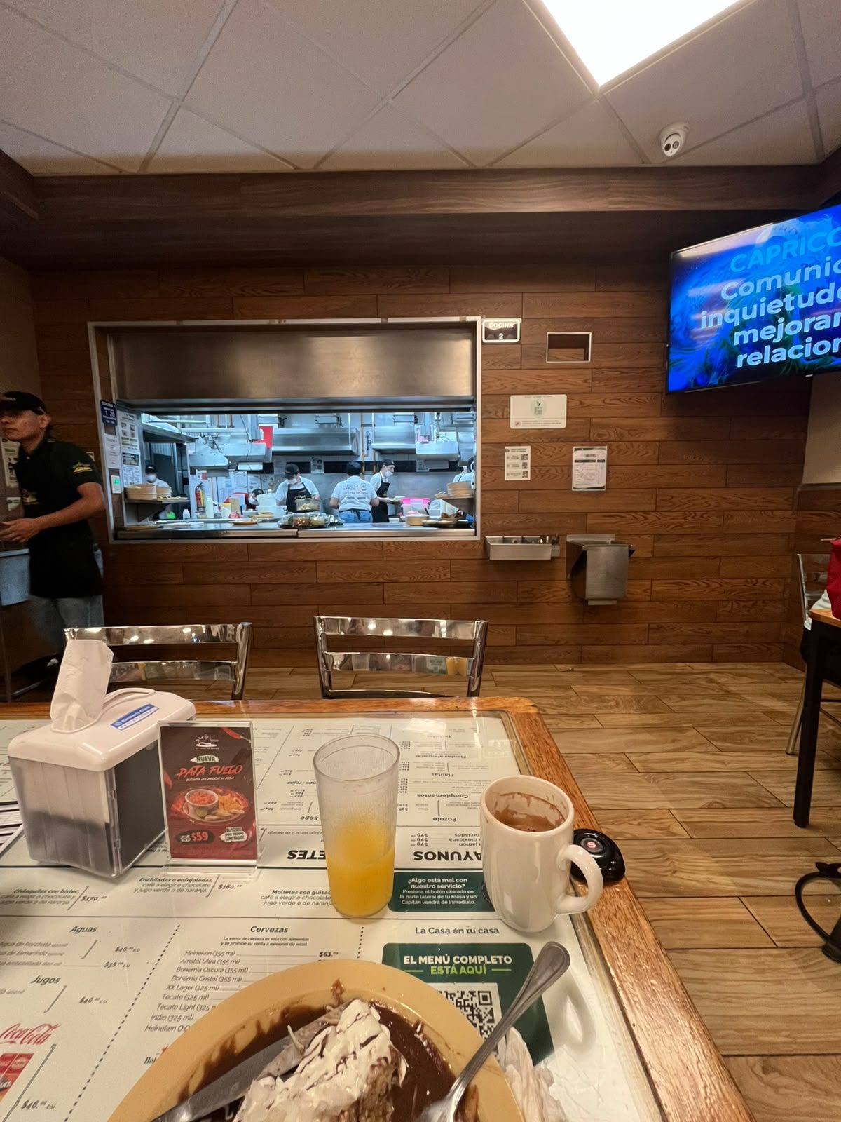 Interior de La Casa de Toño con la cocina abierta al fondo y cocineros preparando platillos