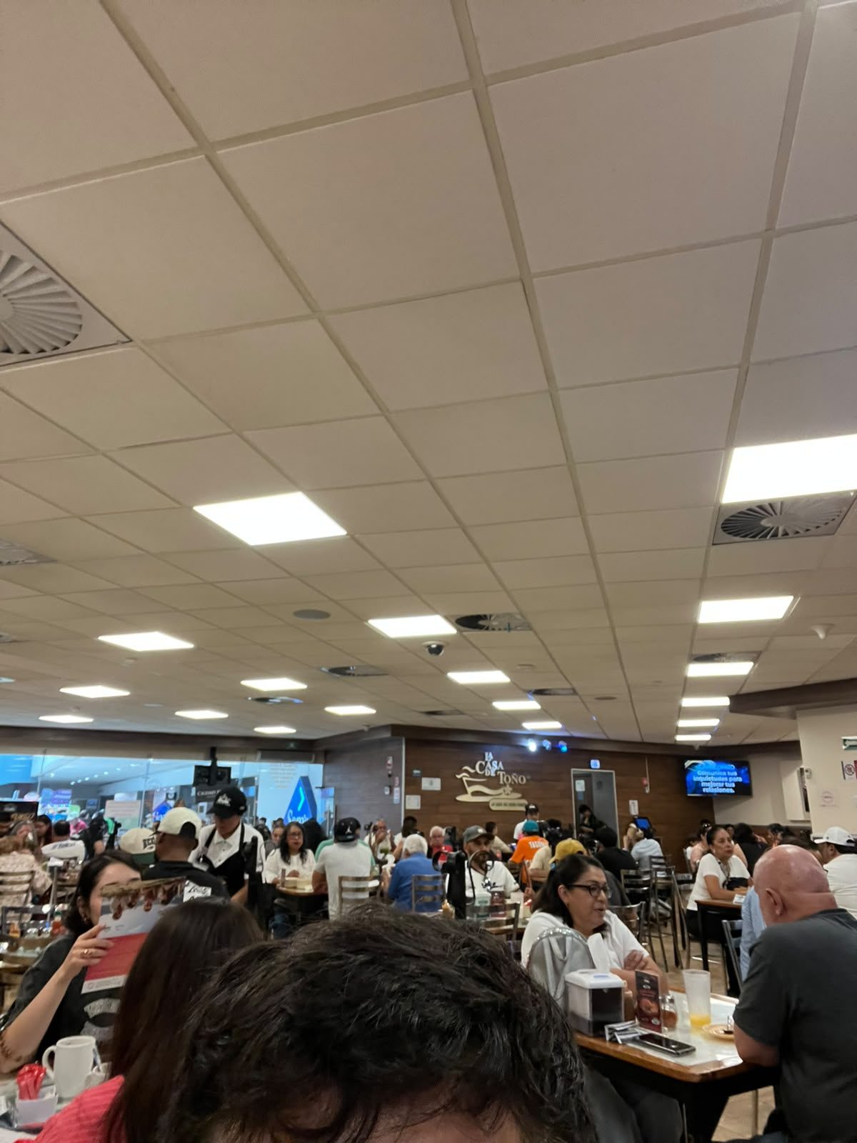 Salón lleno de comensales en La Casa de Toño con el logo del restaurante al fondo