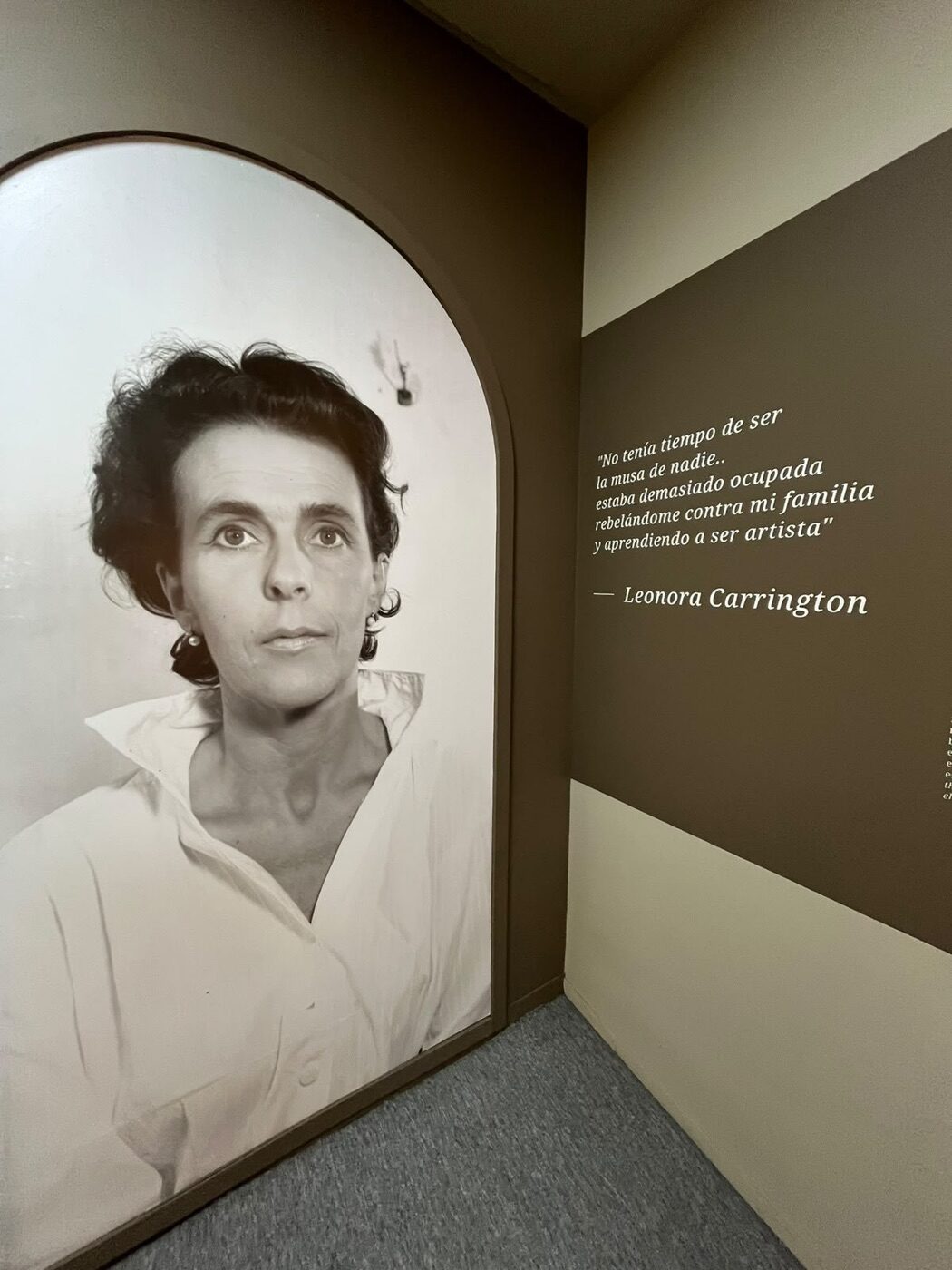 Retrato en blanco y negro de Leonora Carrington junto a su frase «No tenía tiempo de ser la musa de nadie» en la pared de la exposición