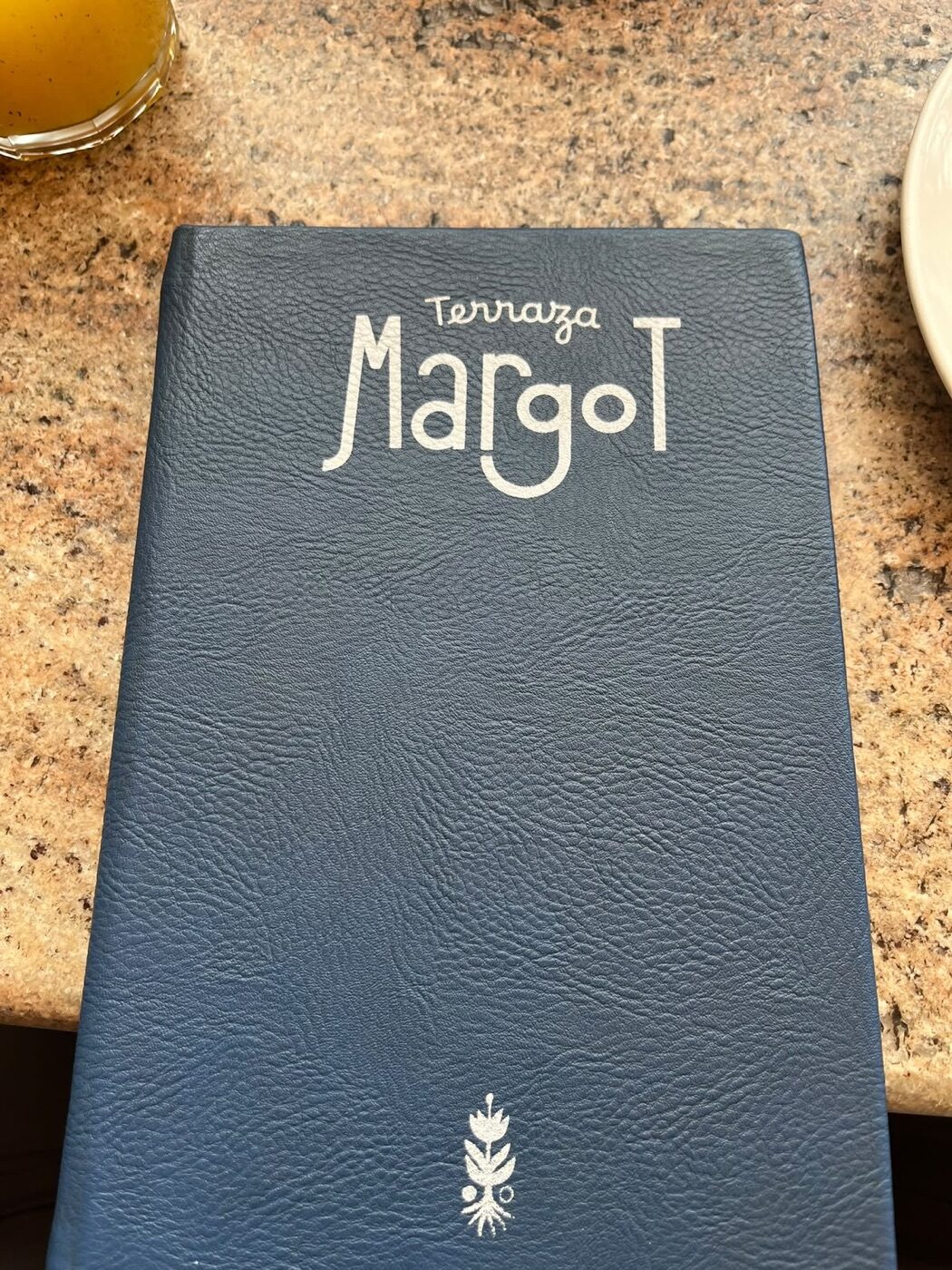 Carta de piel azul de Terraza Margot con el logotipo en blanco sobre la mesa de granito