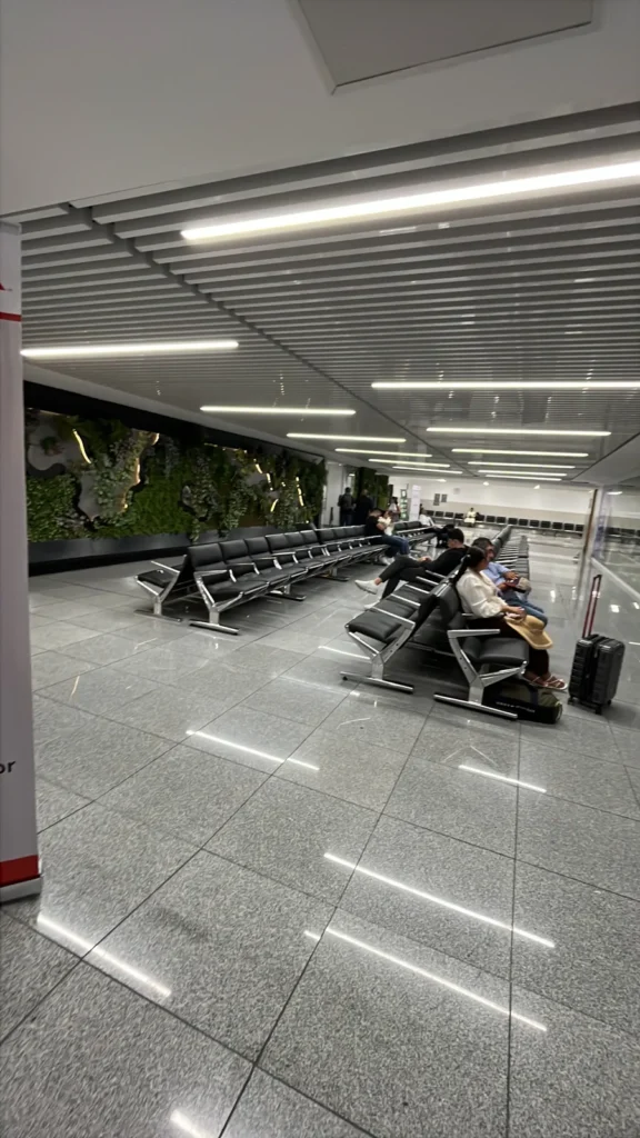 Sala de espera de la Terminal 1 del AICM con asientos y una pared verde