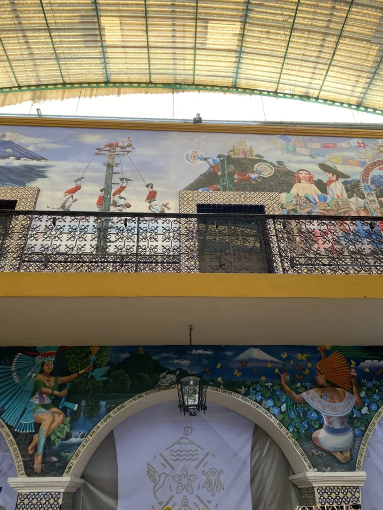 Murales con voladores, un volcán y figuras prehispánicas sobre un balcón de herrería en Atlixco
