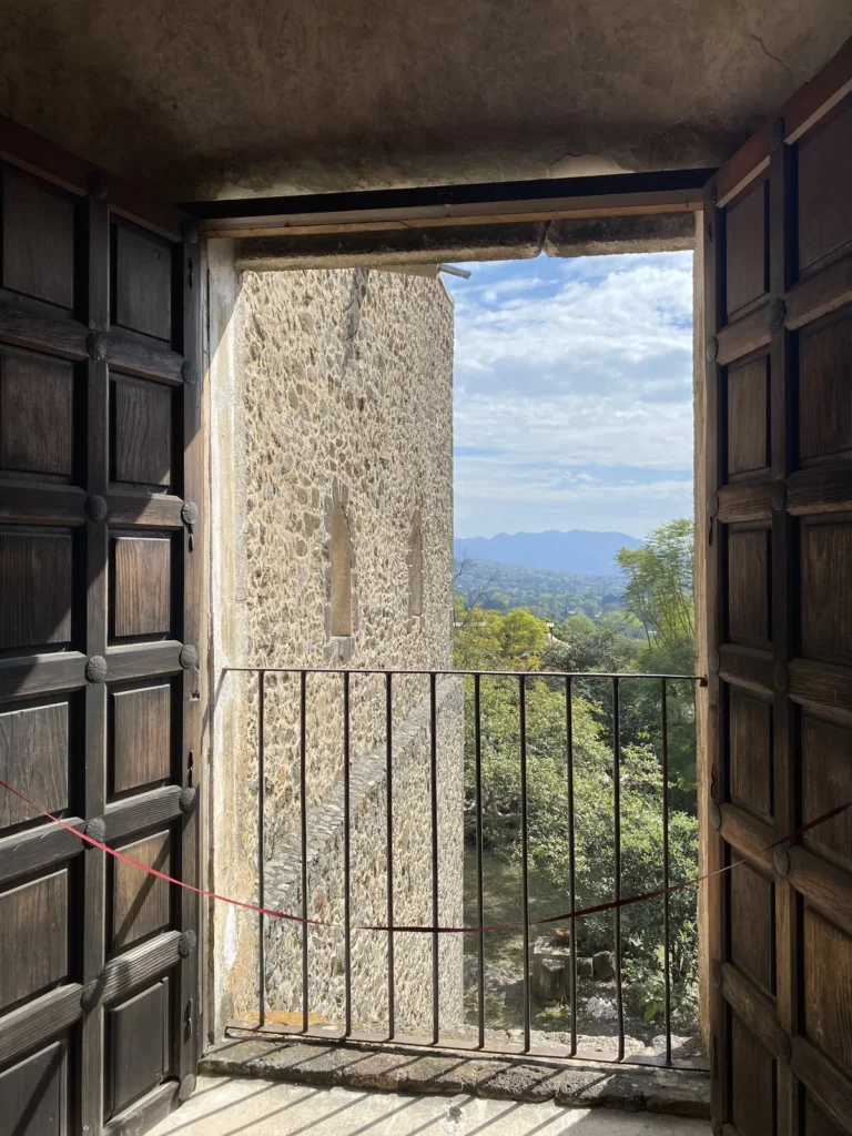 Puerta de madera abierta a un balcón con barandal y vista a cerros y árboles en Tepoztlán