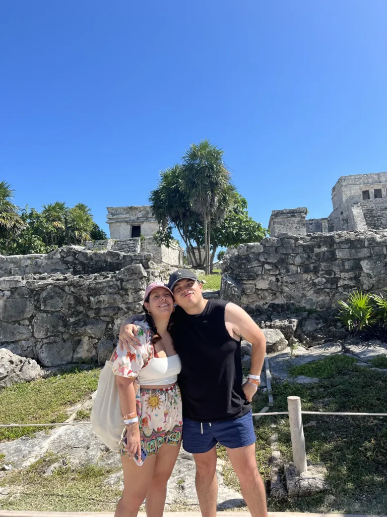 Pareja frente a la muralla de piedra con El Castillo al fondo en la zona arqueológica de Tulum
