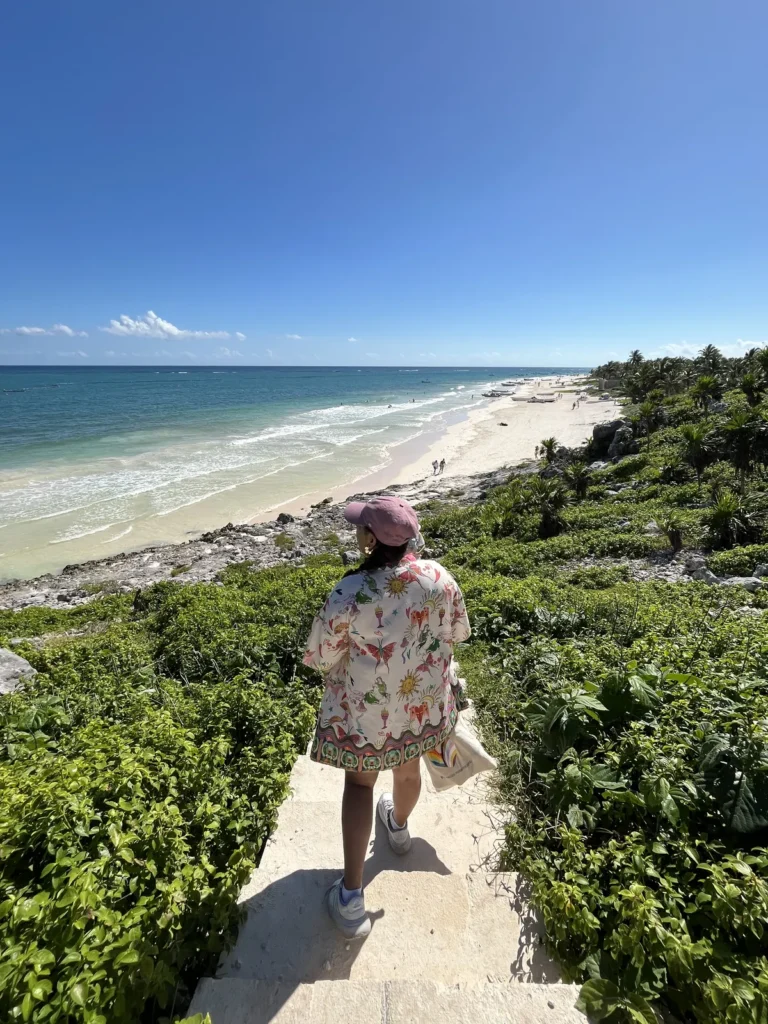 Sendero de arena entre vegetación que baja hacia la playa con la costa de Tulum al fondo