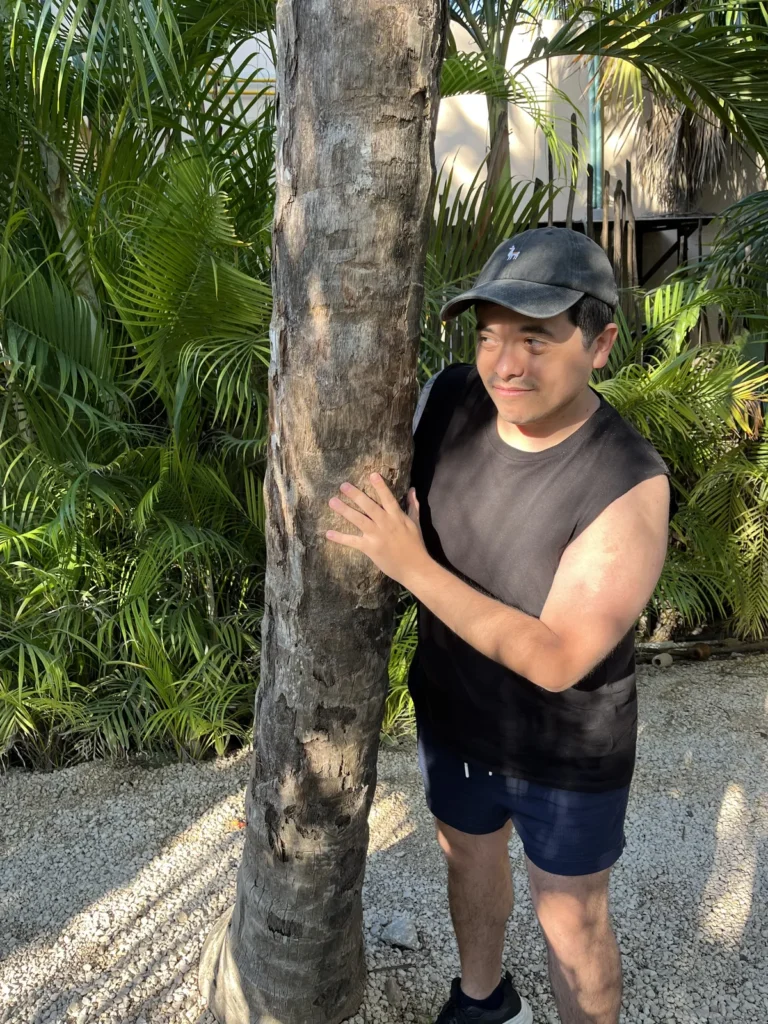 Hombre junto a una palmera en un club de playa de la zona hotelera de Tulum