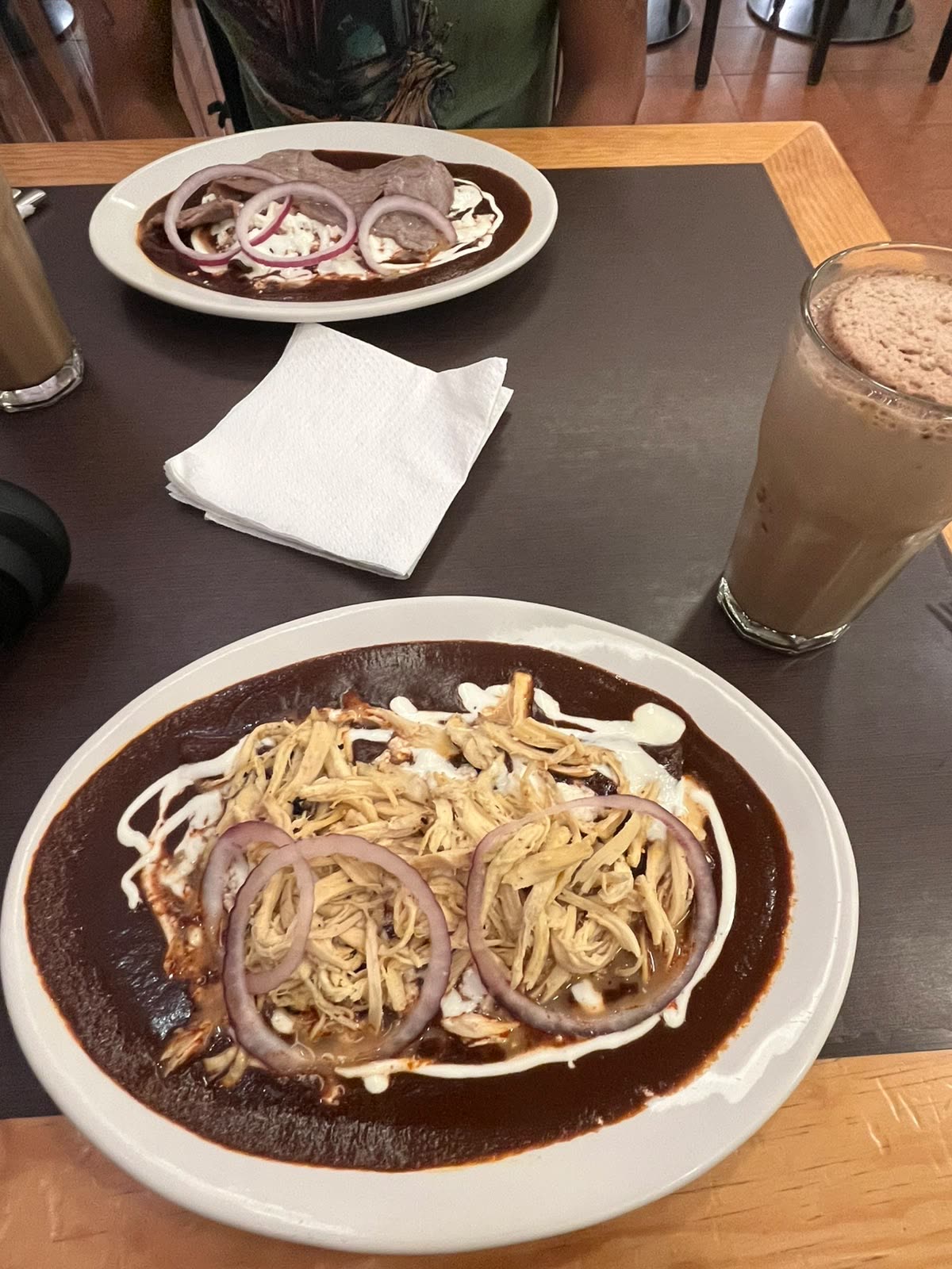 Dos platos de enmoladas bañadas en mole con pollo deshebrado, cebolla y crema, junto a un café con chocolate helado en Mayordomo, Centro de CDMX